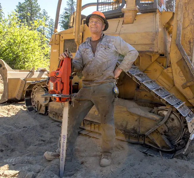 man with chainsaw in front of bulldozer