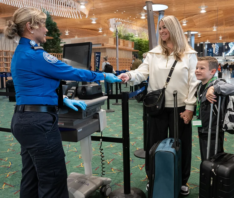 a woman and her son who is wearing a sunflower lanyard provide documents to a TSA agent