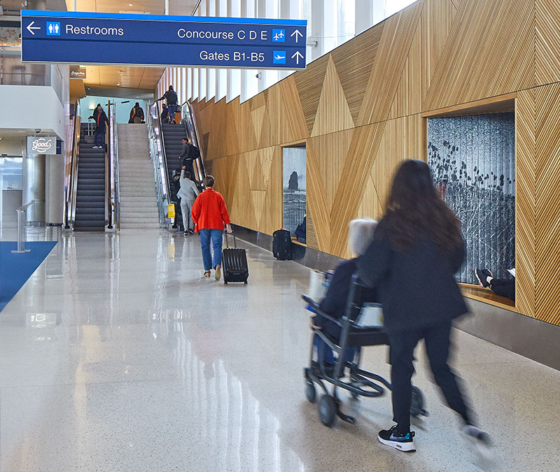 a woman pushing another woman in an airport wheelchair in concourse B