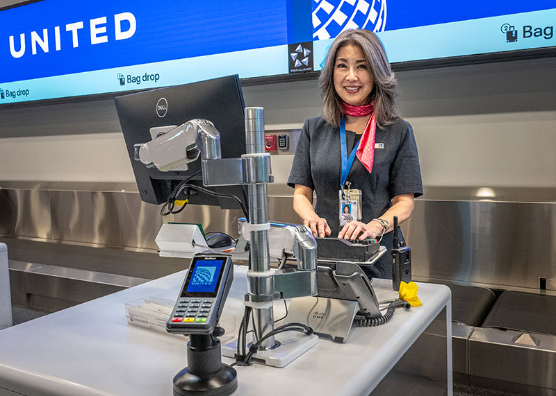 A United Airlines employee is smiling at the ticket counter while typing into the computer
