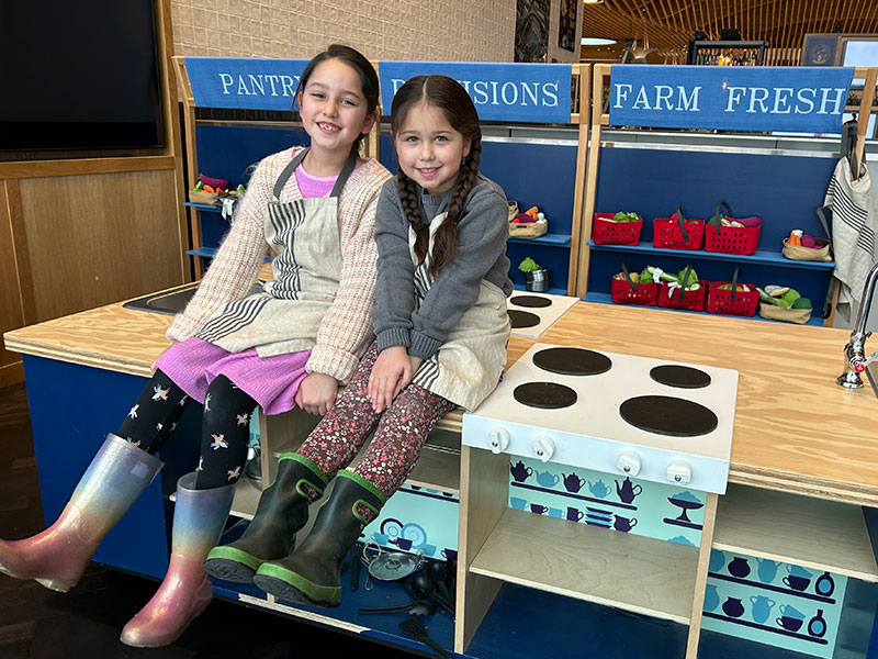 two girls in the Loyal Legion play area smiling atop a play kitchen