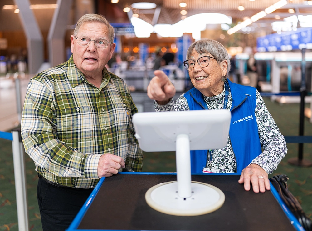 a PDX volunteer wearing a blue vest assists a customer by pointing for directions
