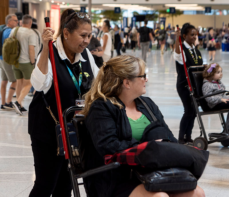 a staff member pushes a traveler in a Wheelchair Assistance chair