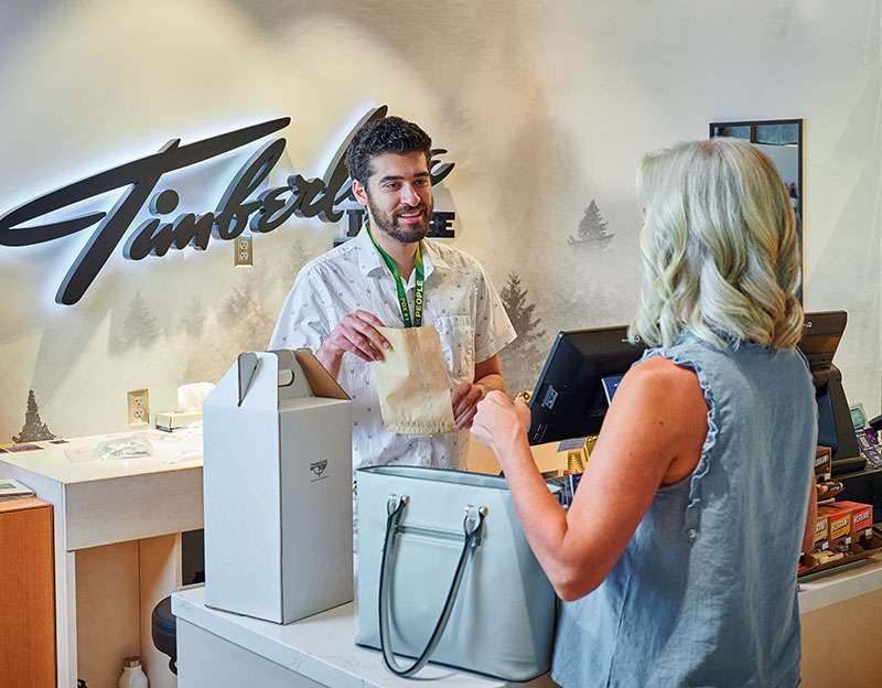 A tall man with dark hair is assisting a white woman with light hair at the cash register of the Timberline store
