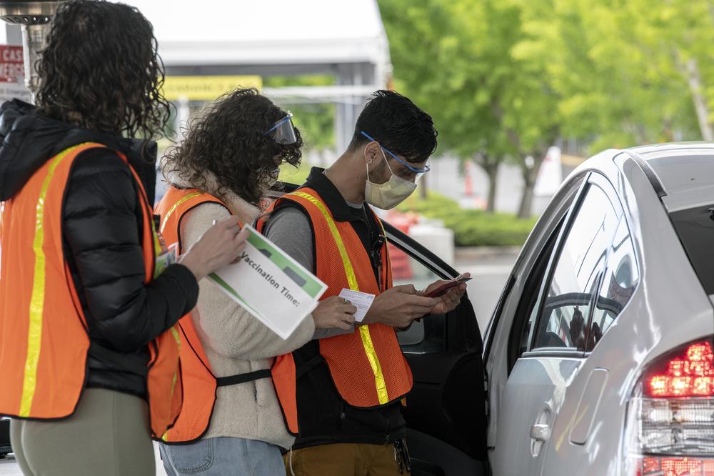 Three OHSU staff members in orange safety vests talk to a vaccine recipient in their vehicle