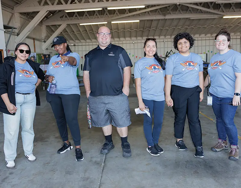 six members of the Port of Portland Community Impact team smile at the camera during a community event at Hillsboro Airport