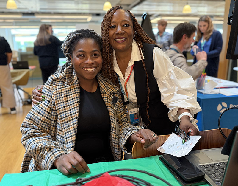 two Black women pose hugging behind a table during a tabling event for the Port of Portland Employee Resource Groups