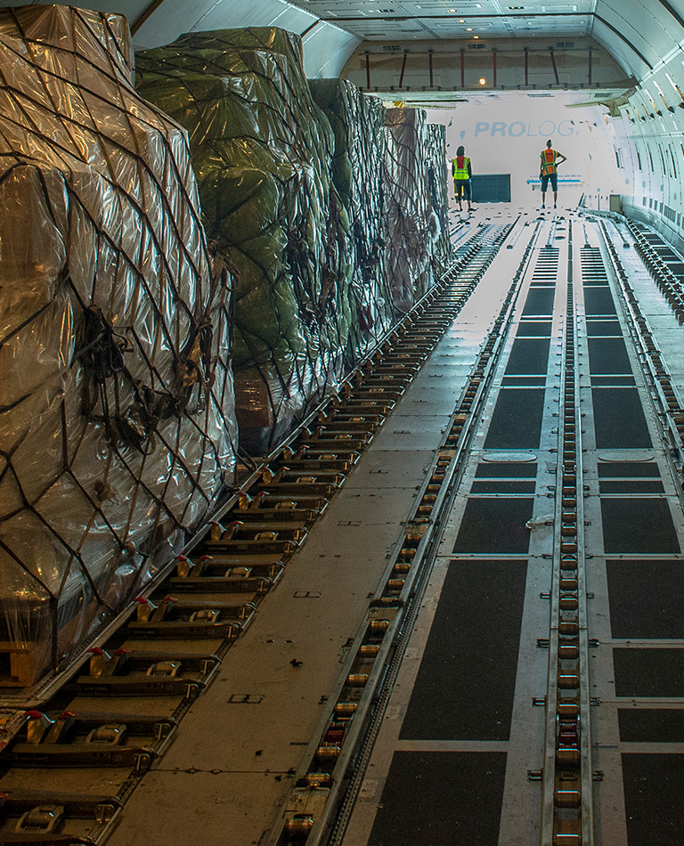 man pulling away after dropping off cargo load while woman on scissor lift prepares the load