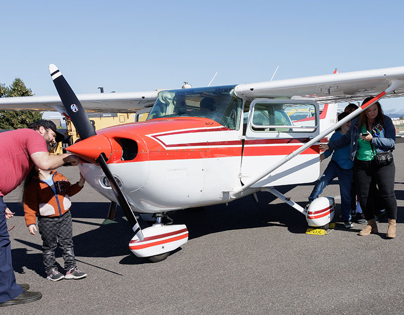 a family of four gathers around a white and red striped small plane