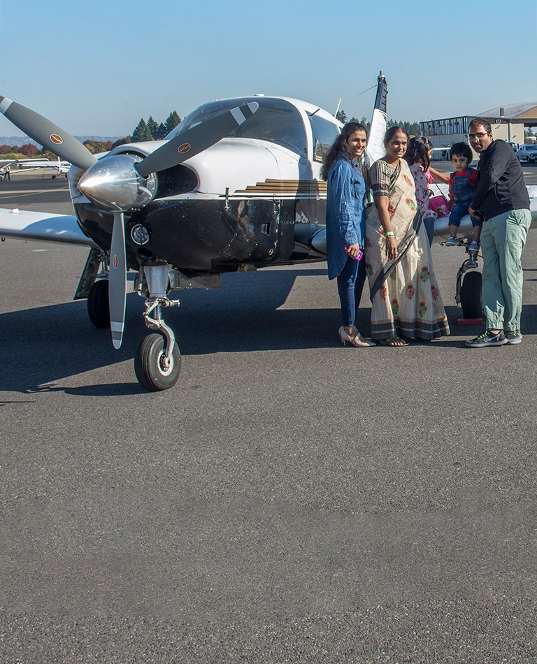 Family of South Asian heritage posing in front of small plane