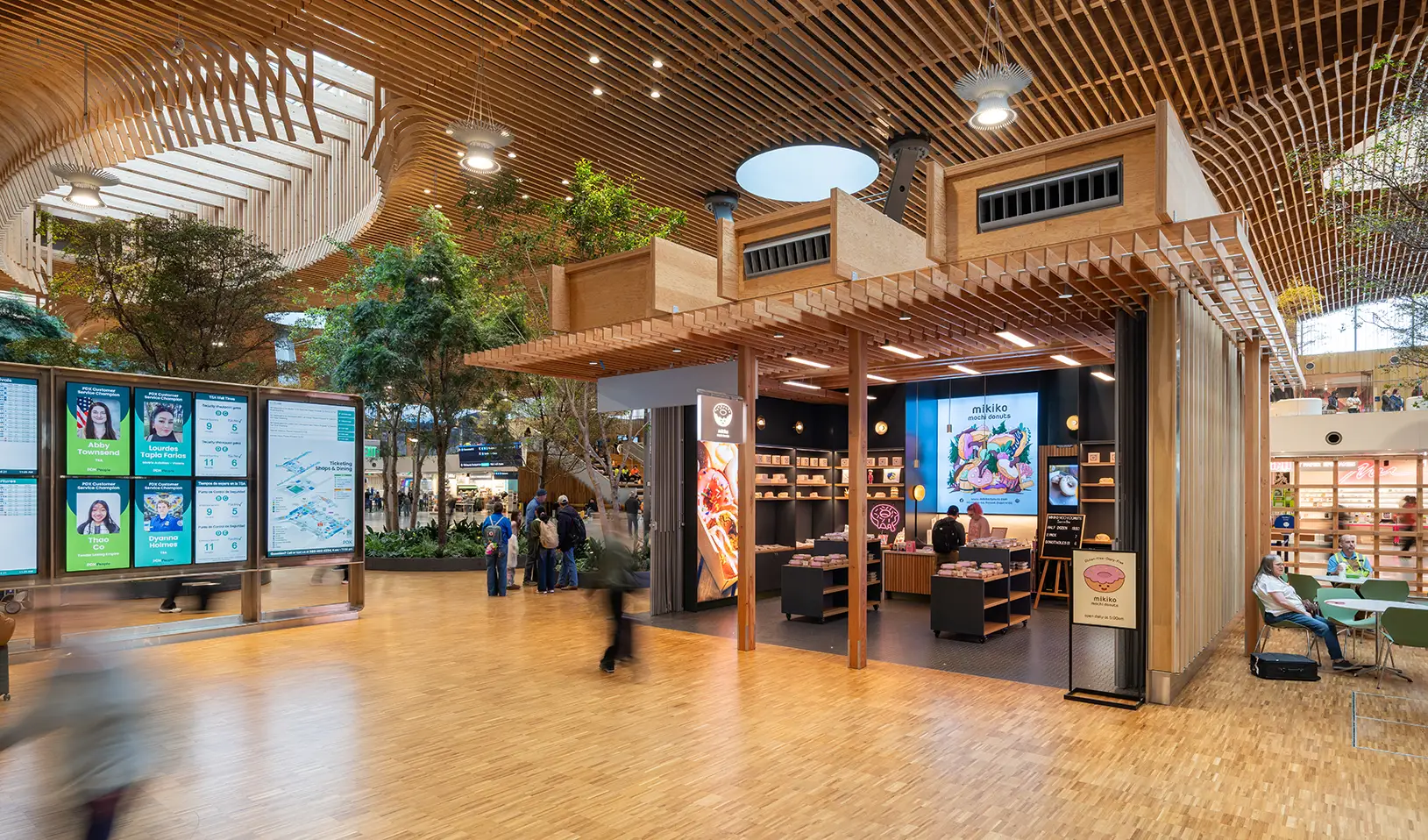 wide exterior of Mikiko Mochi Donuts next to the flight information display monitors in the main terminal while passengers mingle