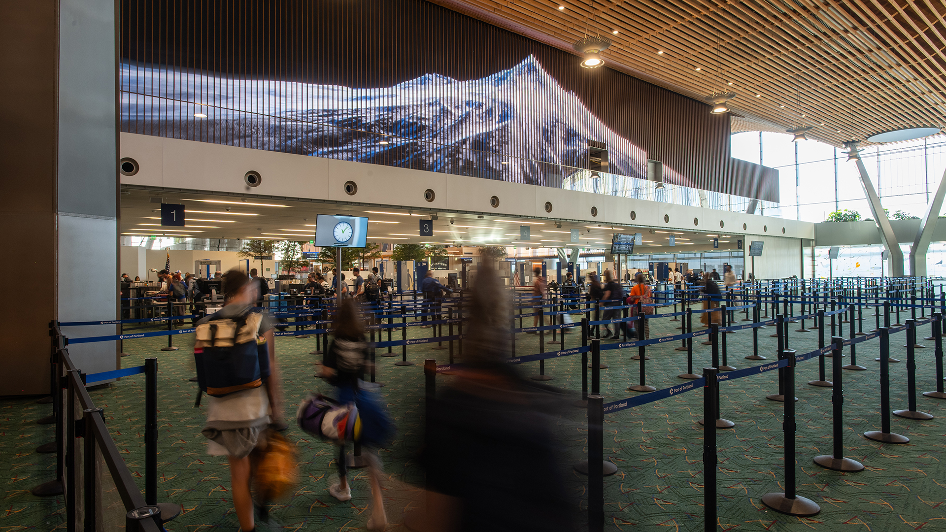 video walls show mountain imagery above busy TSA checkpoint