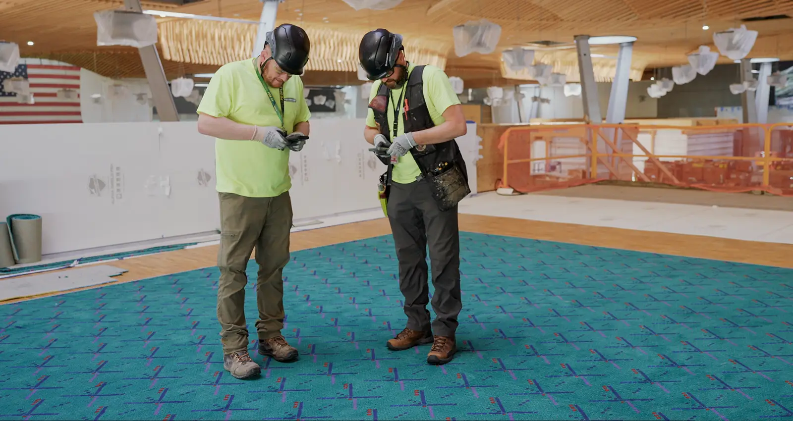 two bearded men in safety gear pause for a shoe selfie after installing the old carpet in new zones in 2024