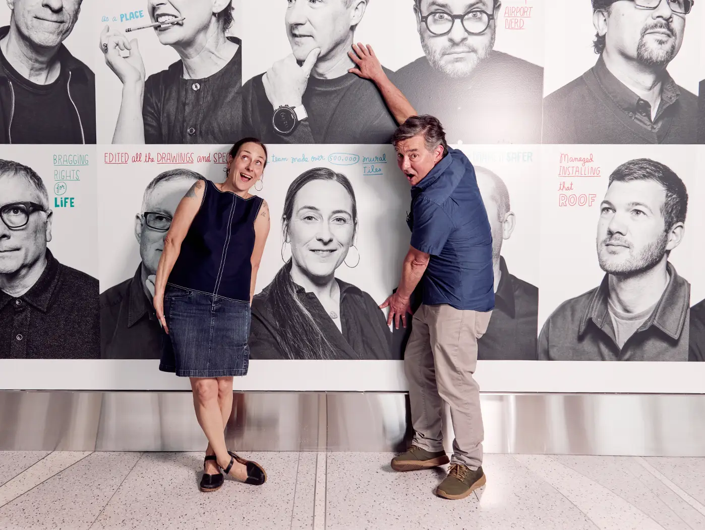 a man and woman make silly faces and poses in front of her portrait within the mural