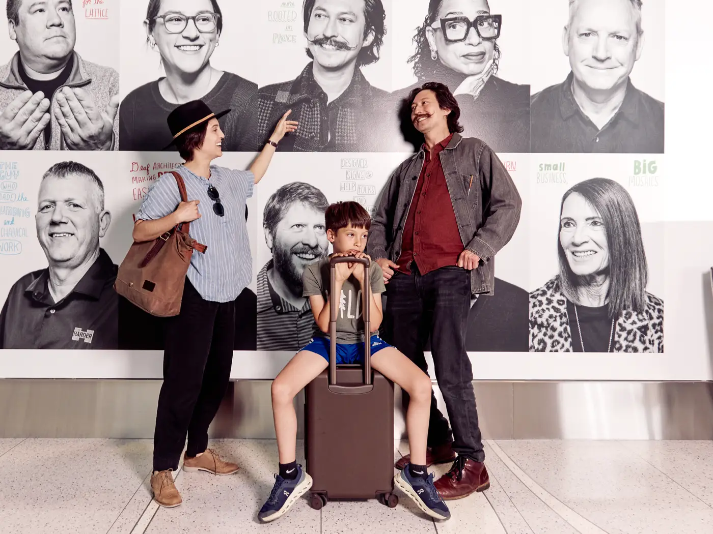 a family stands in front of the father's portrait in the photo while his wife points at his portrait