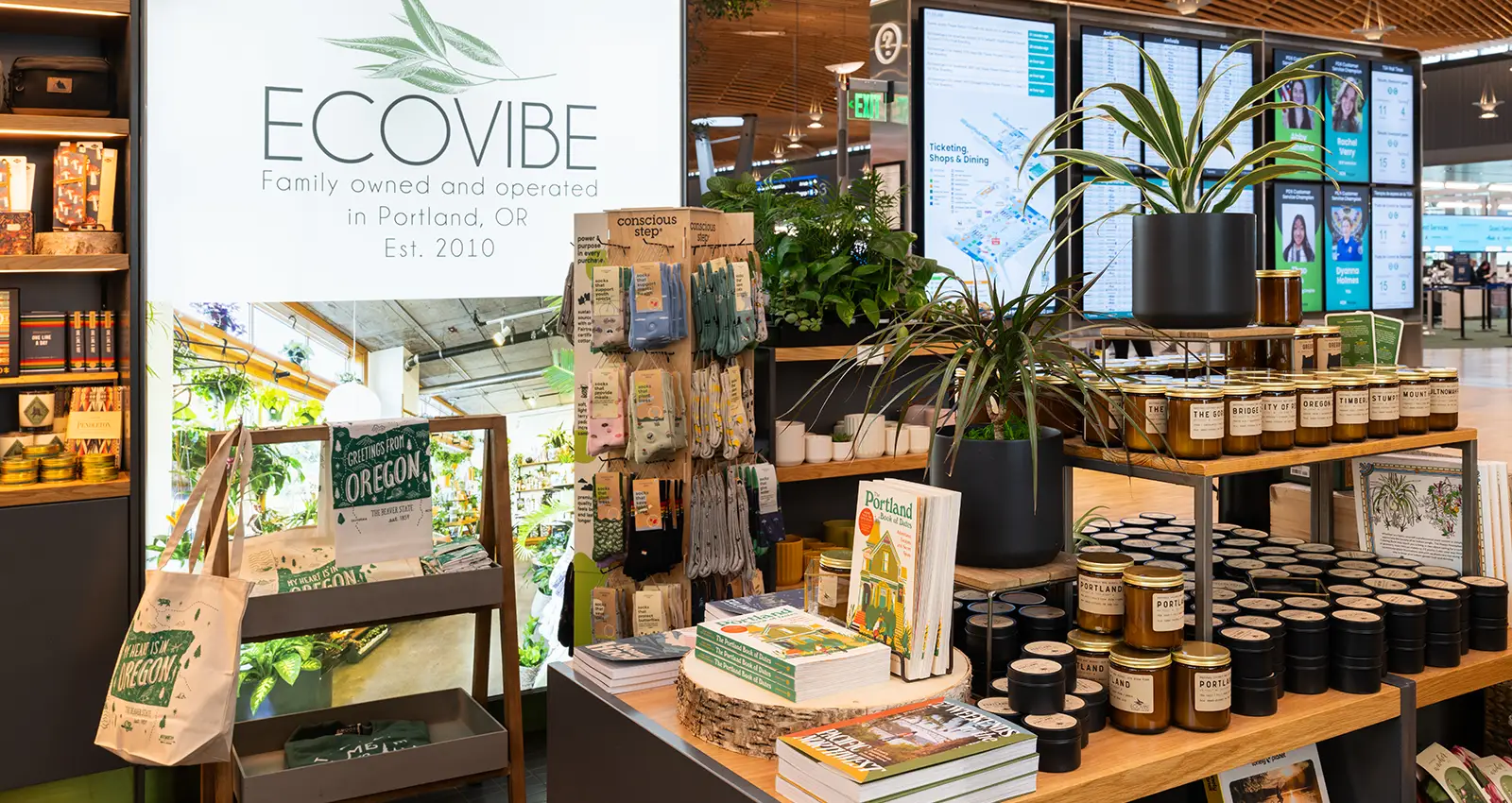 The ECOVIBE sign is illuminated in the background with various gift items such as socks, books, and candles in the foreground