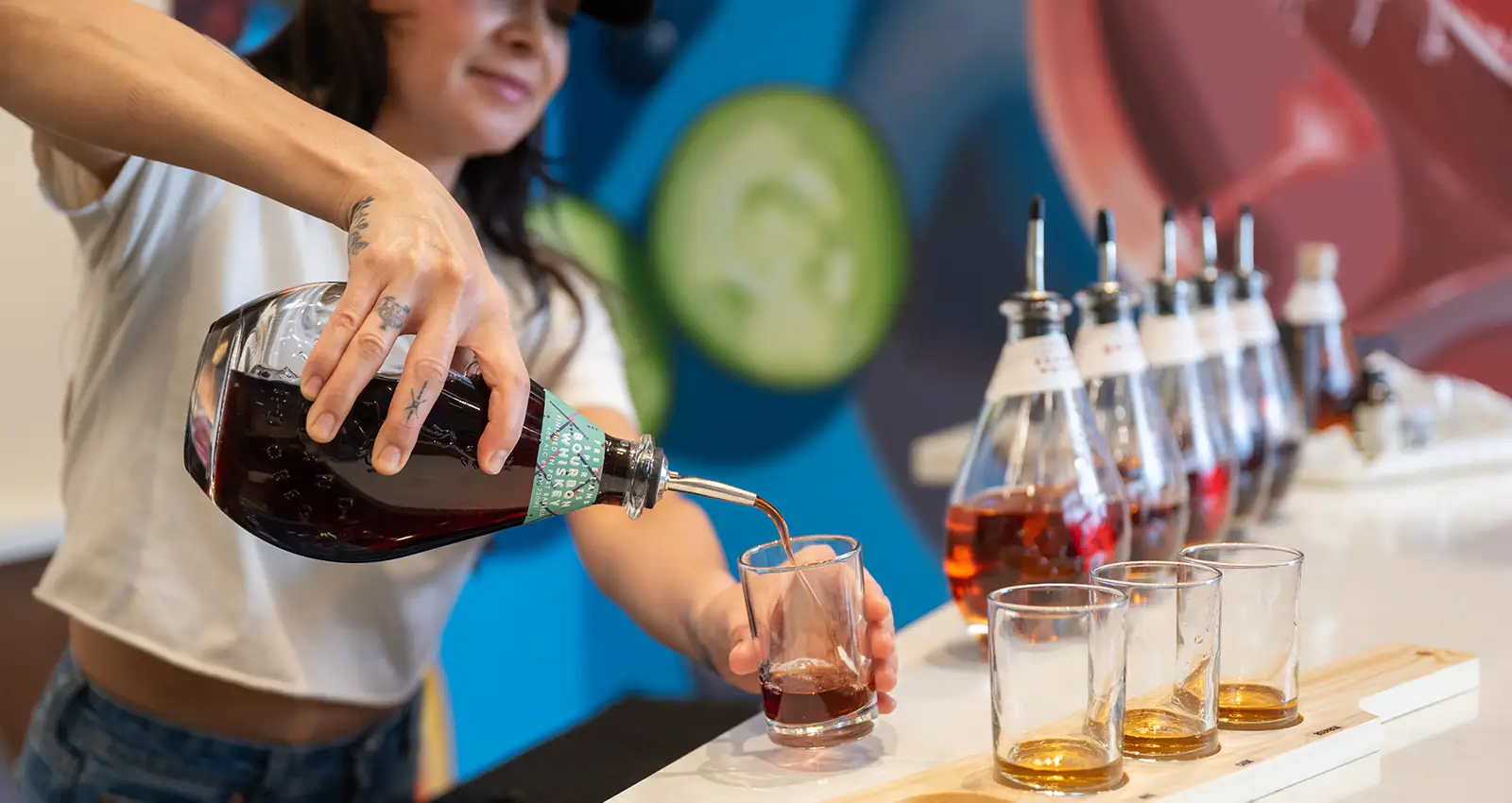 a woman pours the PDX specialty bourbon into a flight of various whiskeys