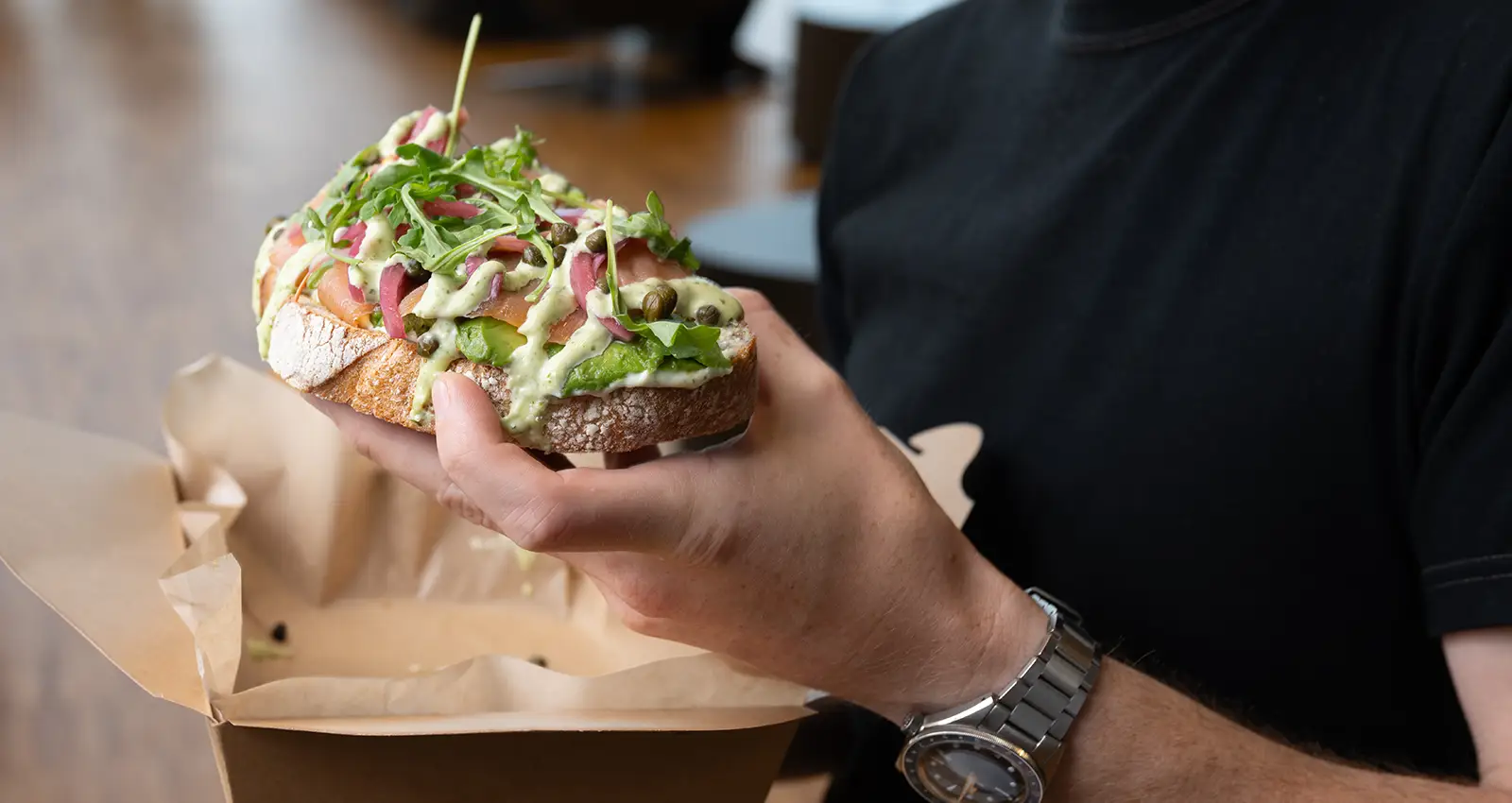 a close shot of a man's hand holding a salmon lox covered toast from Lolas