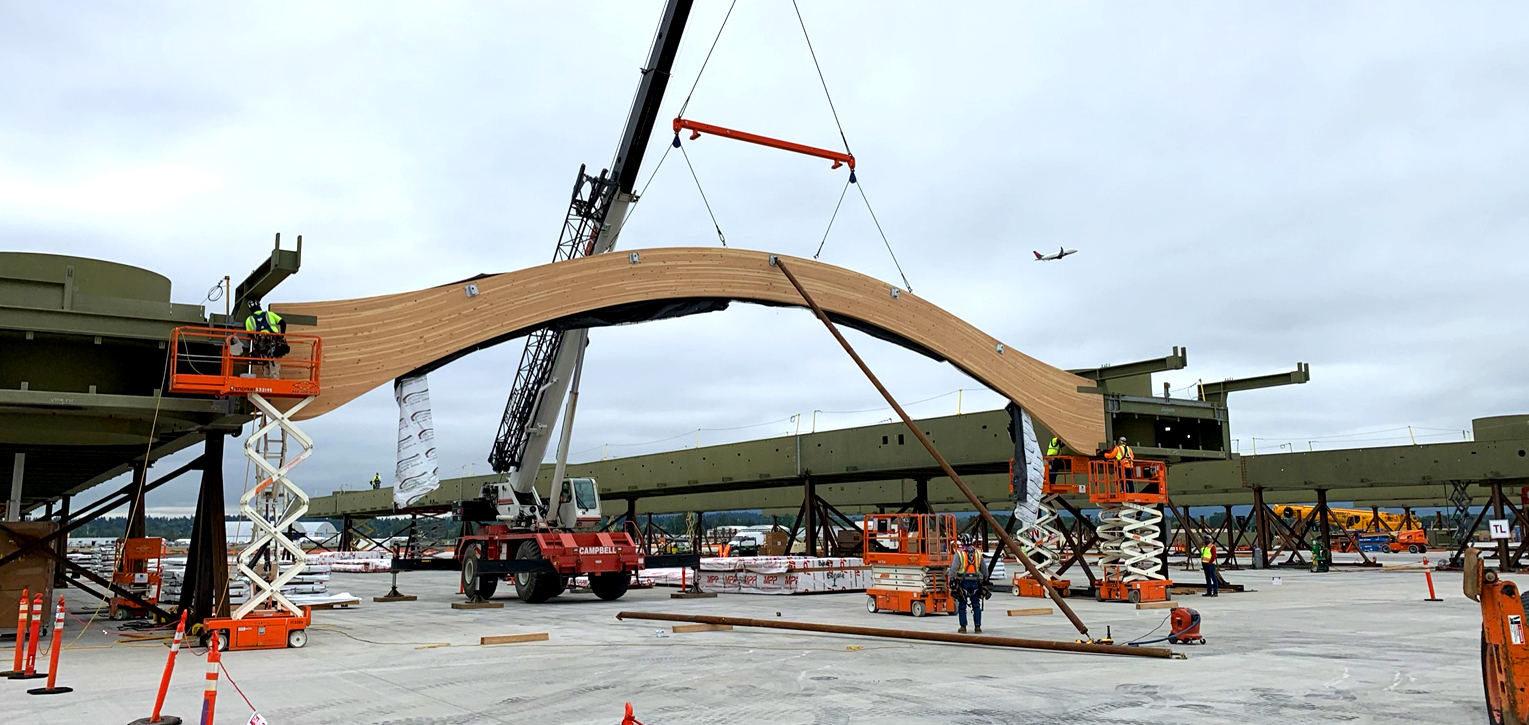 A crane helps slide a curvy beam into a segment of the new roof