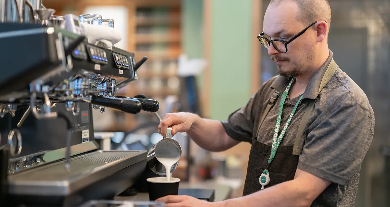 a Smith Tea employee wearing glasses pours steamed milk into a specialty beverage